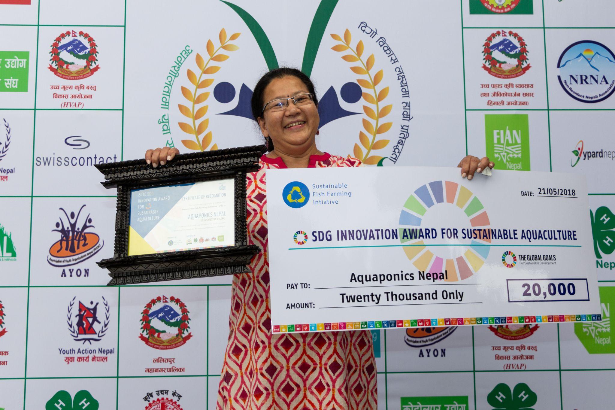 Rita Shrestha Bhadra holds an SDG Innovation Award check and certificate for Aquaponics Nepal.
